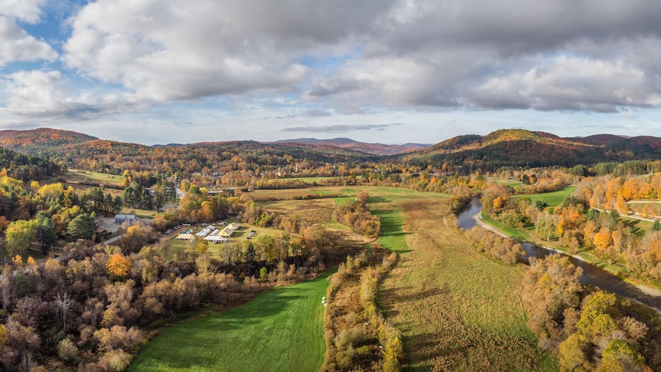 A valley with a river, surrounded by autumn-colored trees and rolling hills.