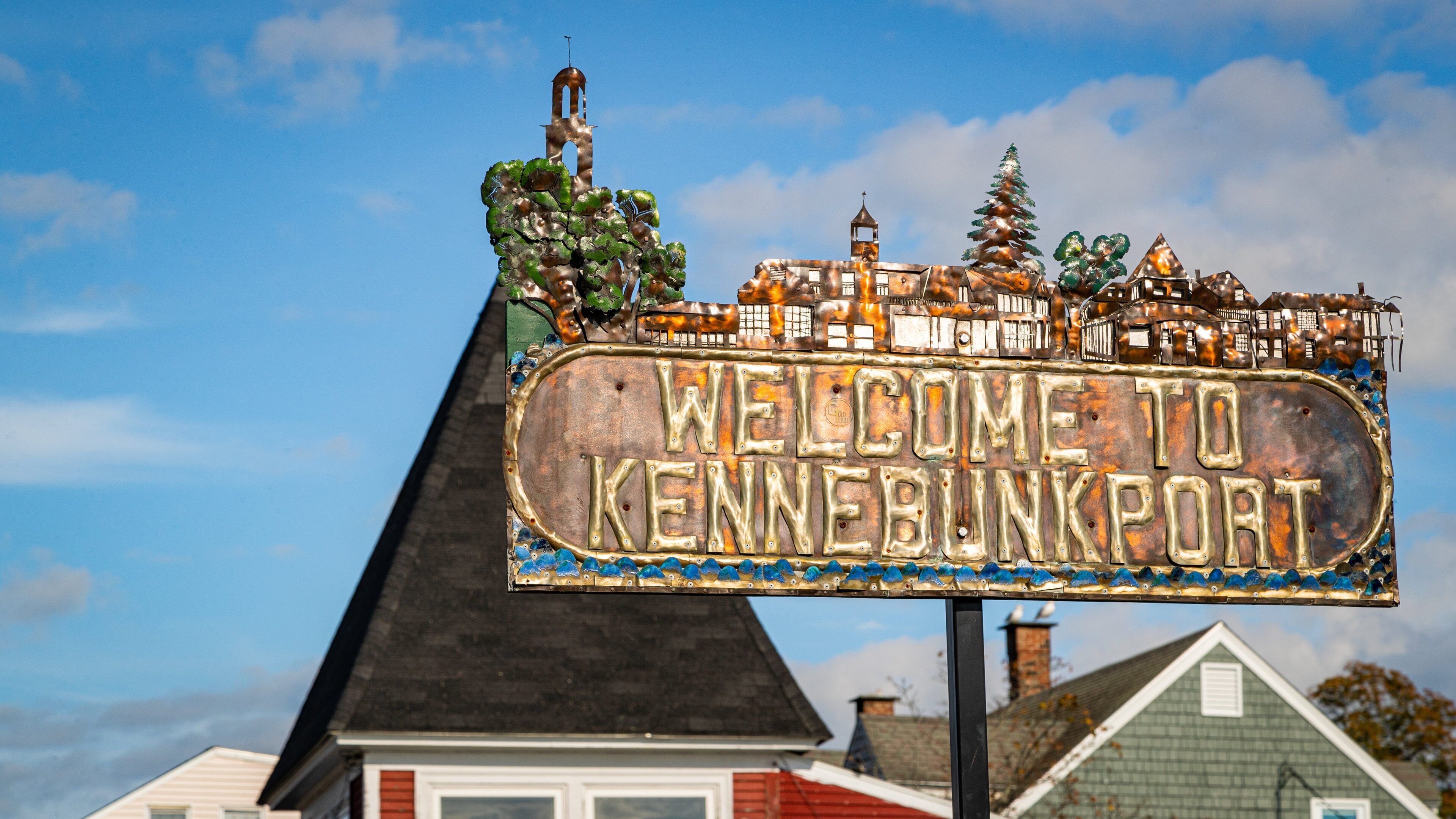 A weathered welcome sign with a rustic design, featuring a church steeple and a Christmas tree.