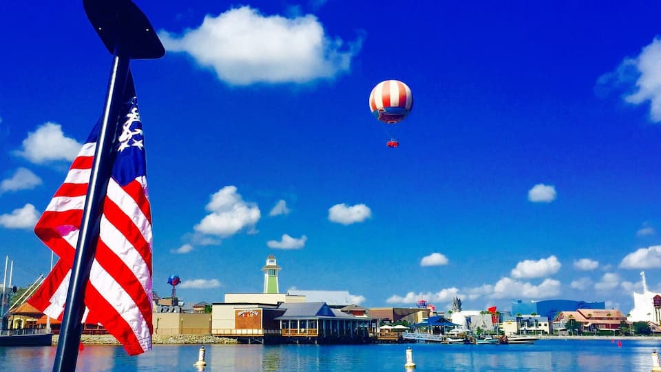 A clear blue sky with a hot air balloon, a flag, and a waterfront with buildings.