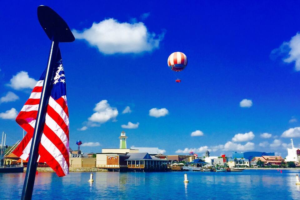 A clear blue sky with a hot air balloon, a flag, and a waterfront with buildings.