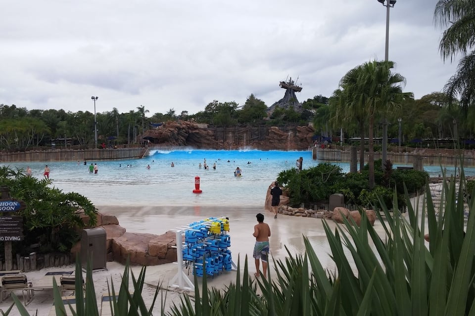 Um parque aquático com uma piscina grande, palmeiras e um cenário rochoso.