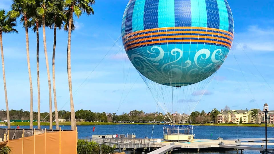 A hot air balloon over a body of water with palm trees and a dock.