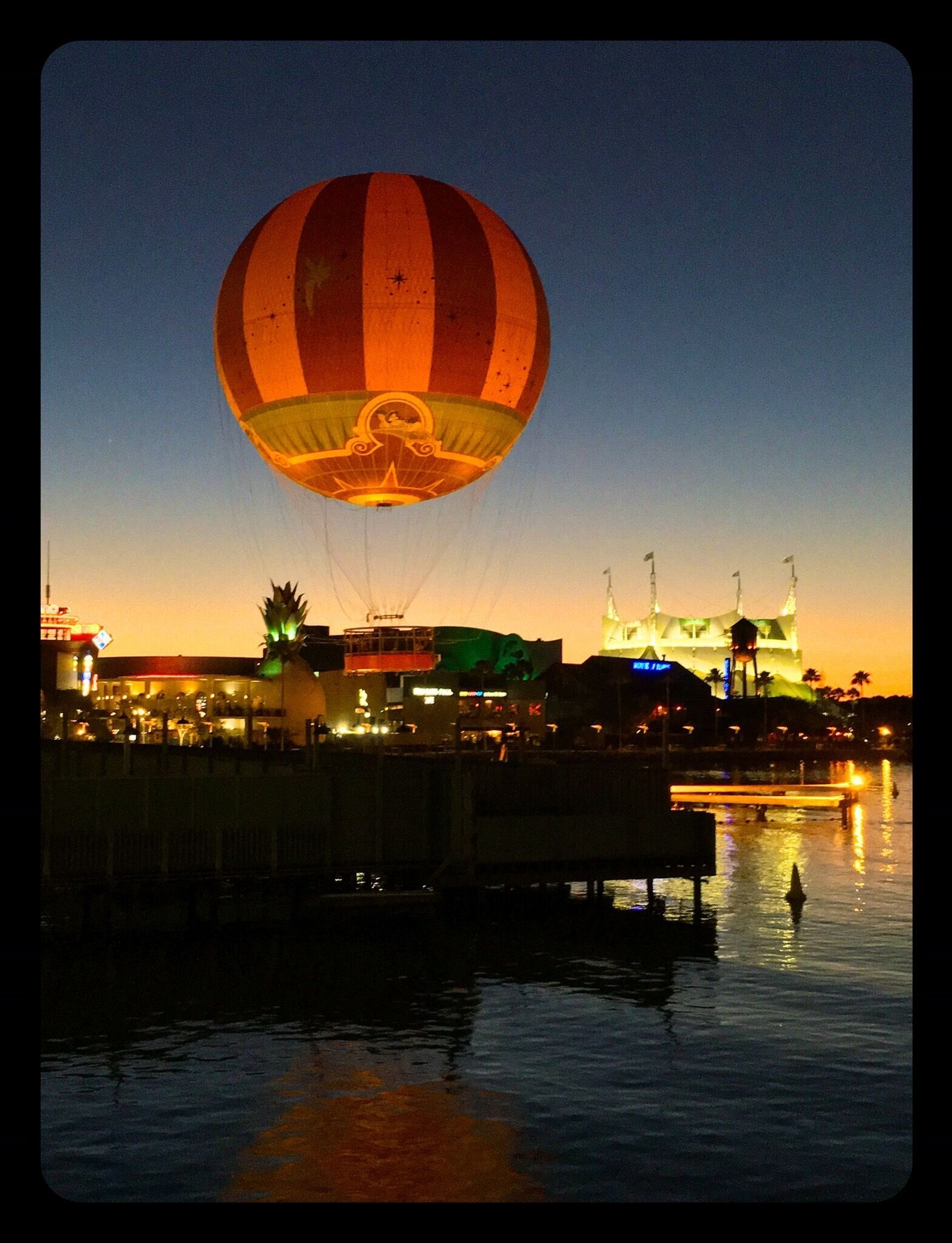 A hot air balloon over a waterfront with illuminated buildings in the background.