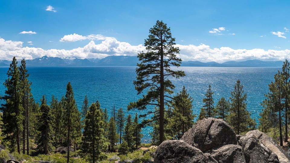 A mountainous landscape with a clear blue lake, surrounded by dense forests and rocky terrain.