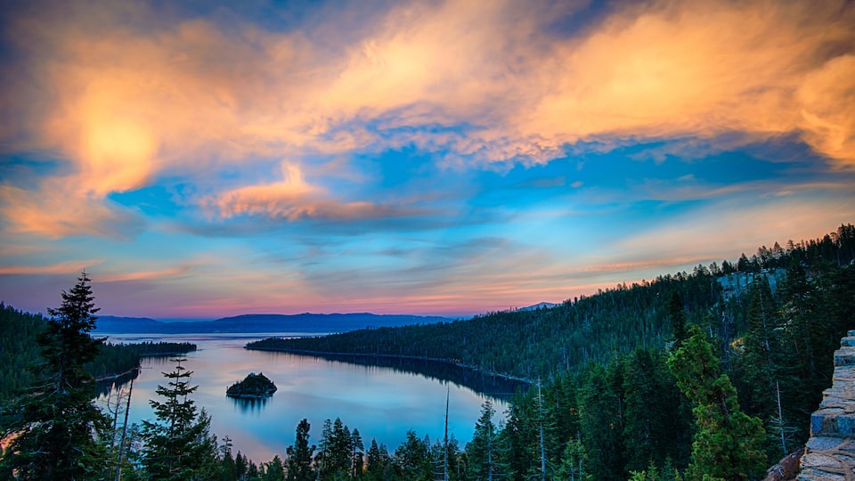 A lake surrounded by dense forest and mountains under a colorful sky.