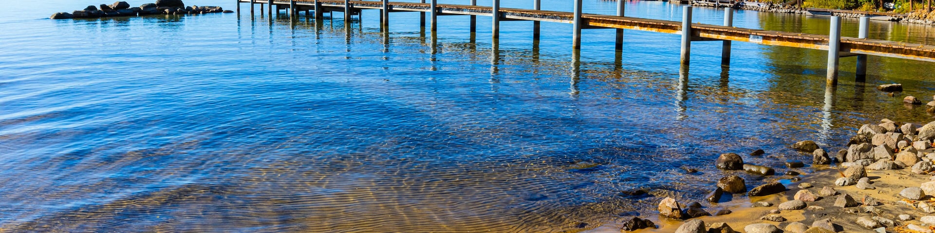 Un lago cristalino con un muelle de madera que se adentra en el agua, rodeado de rocas y árboles.