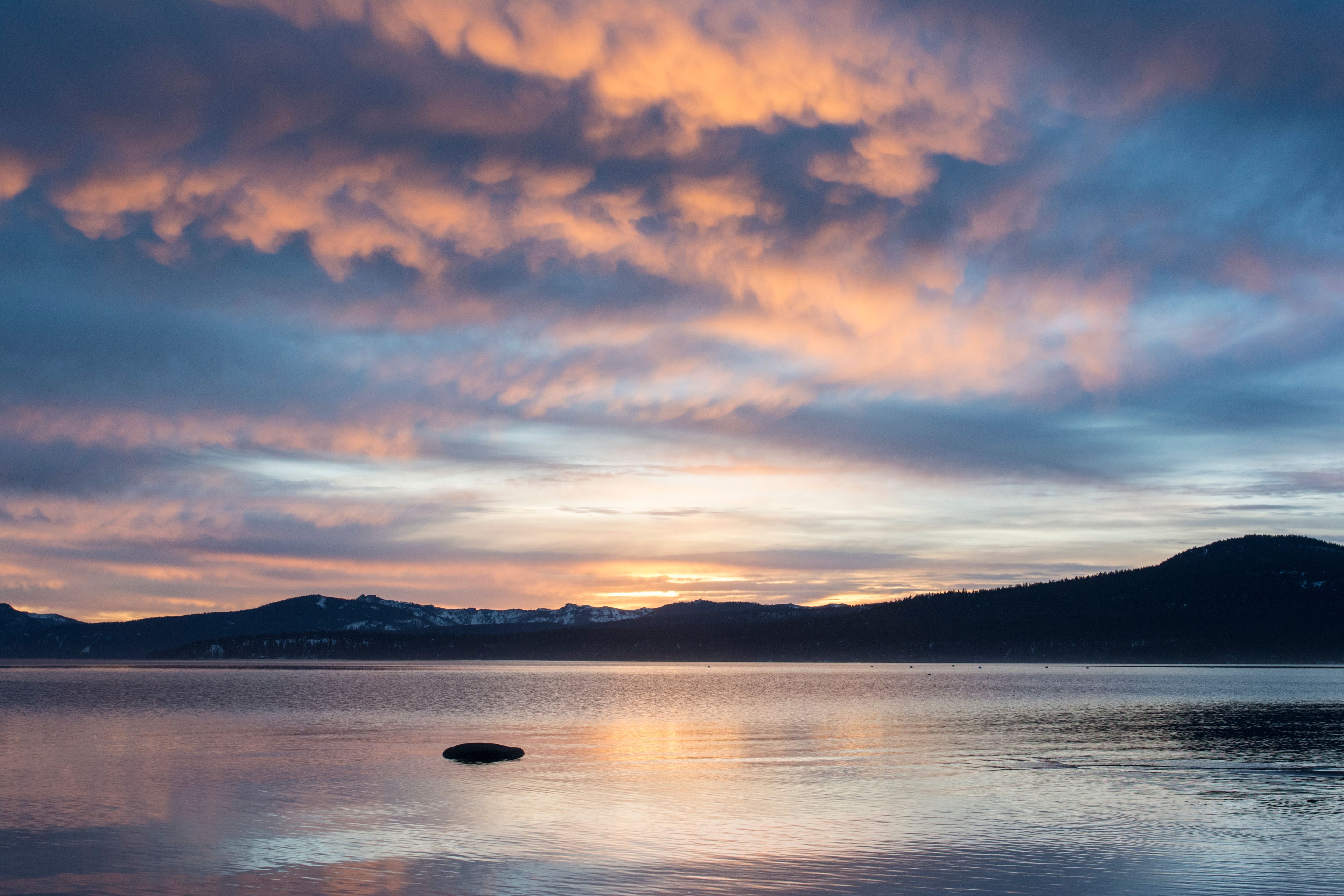 A calm lake with a sunset, mountains in the background, and a small island in the center.