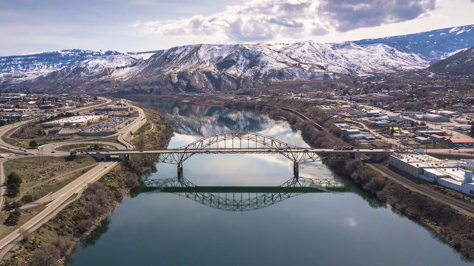 A snow-covered mountain range, a bridge over a river, and a town with buildings and roads.
