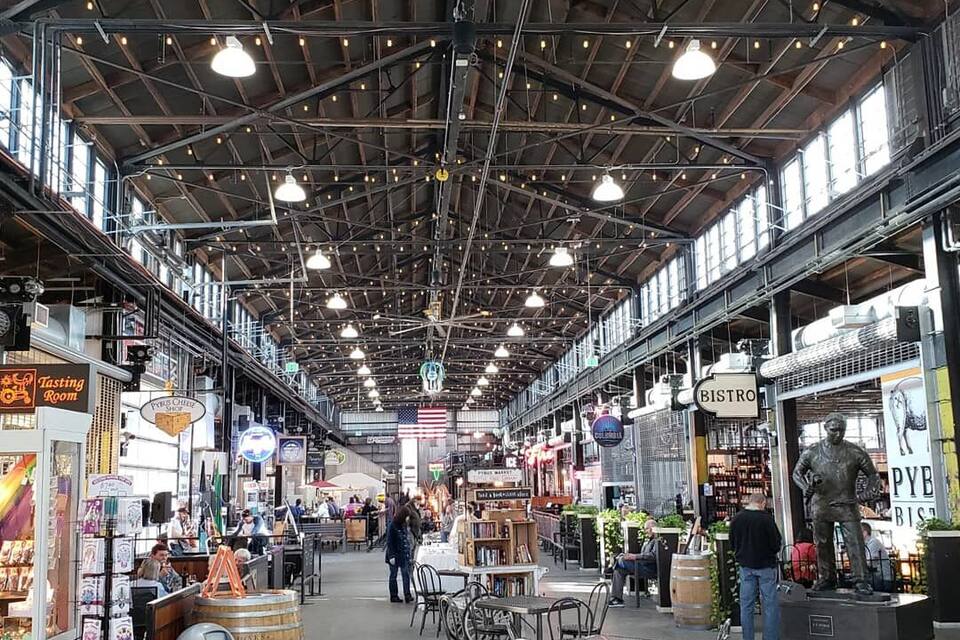 An indoor market with wooden barrels, tables, and chairs. There are signs for a tasting room and a bistro.