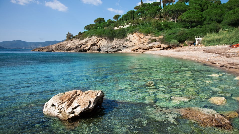 A clear coastal beach with rocky shorelines and lush greenery on a hillside.