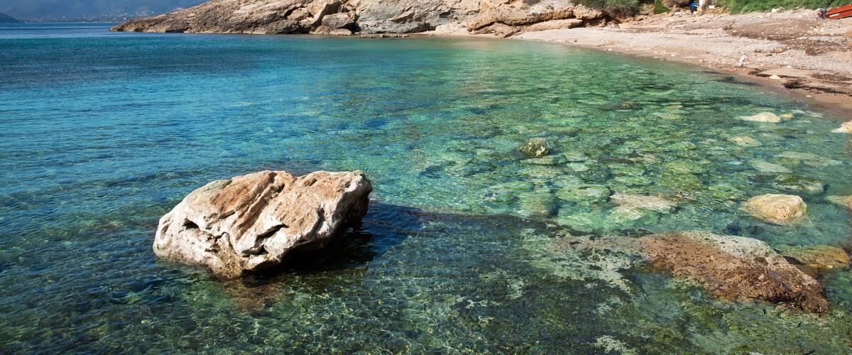 A clear coastal beach with rocky shorelines and lush greenery on a hillside.