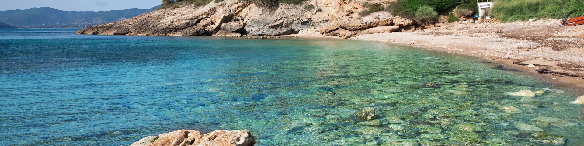 A clear coastal beach with rocky shorelines and lush greenery on a hillside.