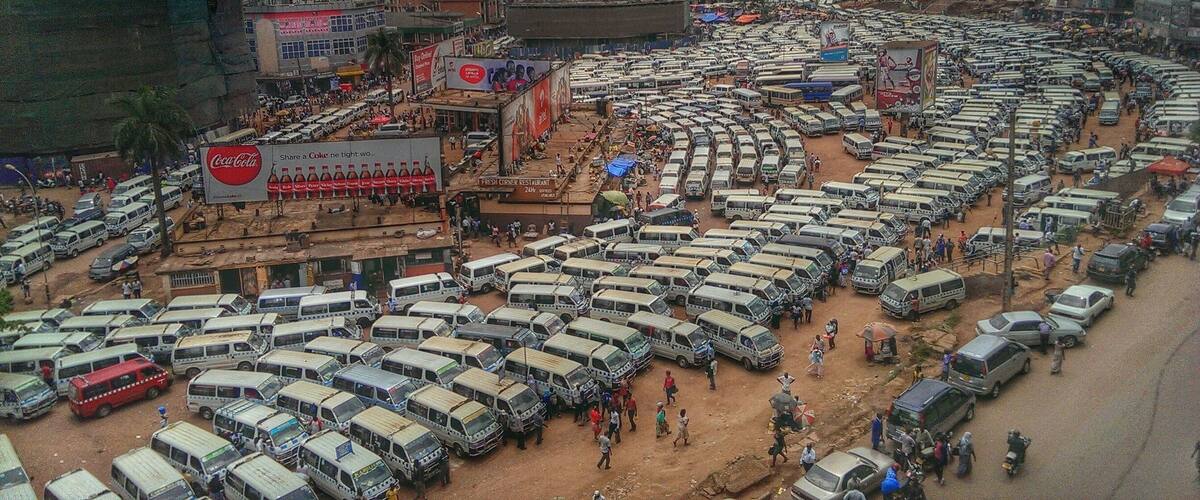 A congested parking lot with numerous buses and cars, a Coca-Cola billboard, and a crowded street scene.