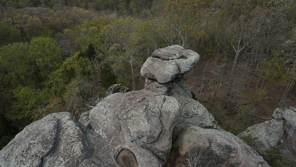 A rocky outcrop with a balanced rock formation in a forested area.