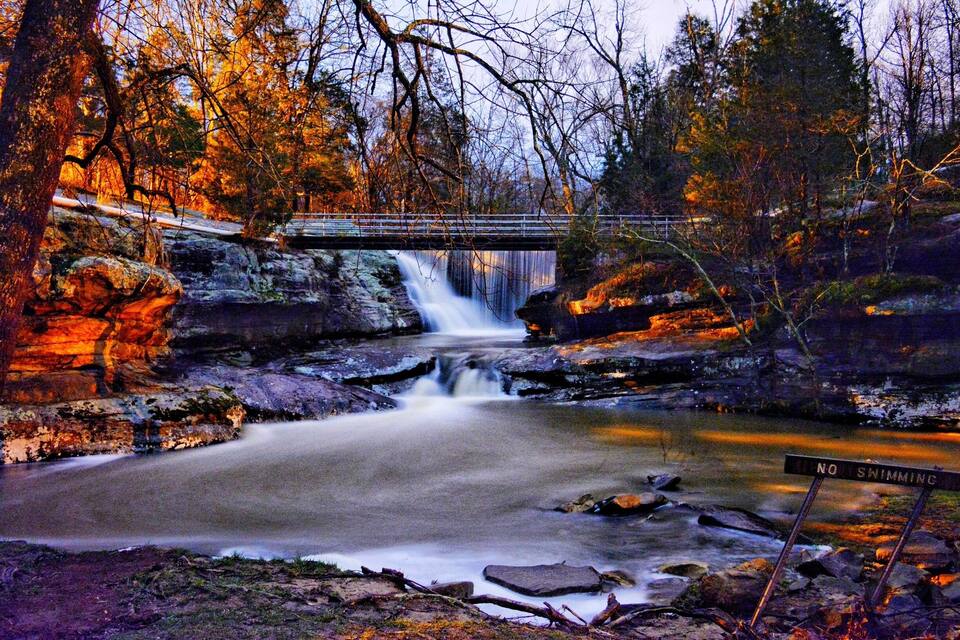 A waterfall, a bridge, and a 'No Swimming' sign in a forested area.