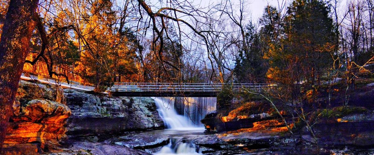 A waterfall, a bridge, and a 'No Swimming' sign in a forested area.
