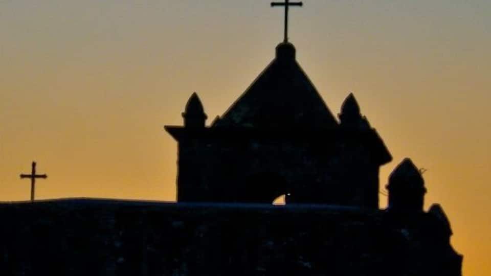 A church silhouette with a cross on top and another on the side of a building during sunset.