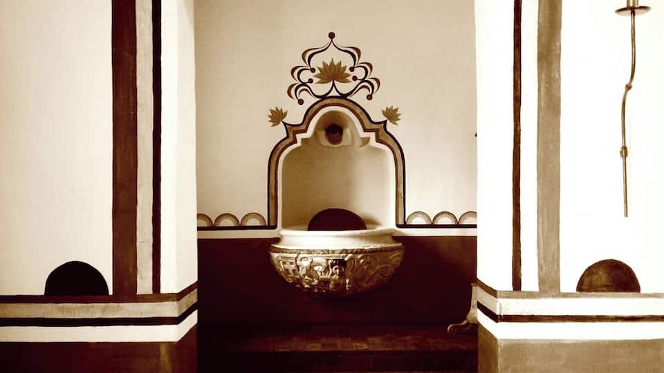 A traditional fountain with intricate designs, a decorative arch, and a wall-mounted light fixture.