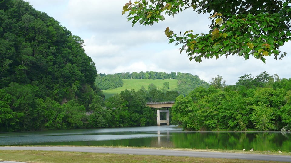 A bridge over a calm lake surrounded by lush greenery and hills.