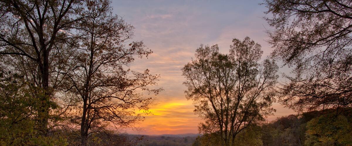 A sunset over a grassy field with trees and hills in the background.