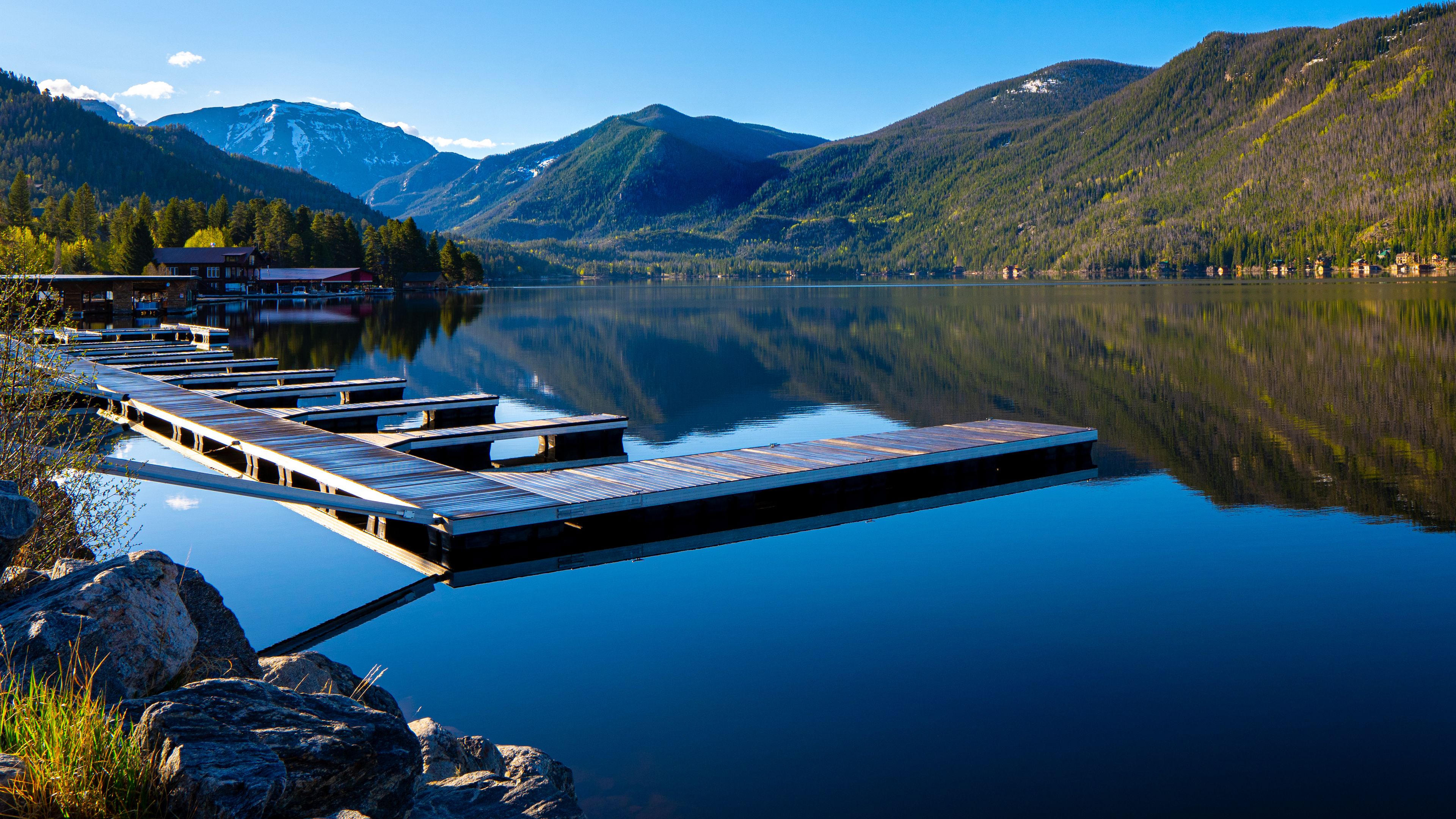 A calm lake with wooden docks extending into the water, surrounded by mountains and trees.