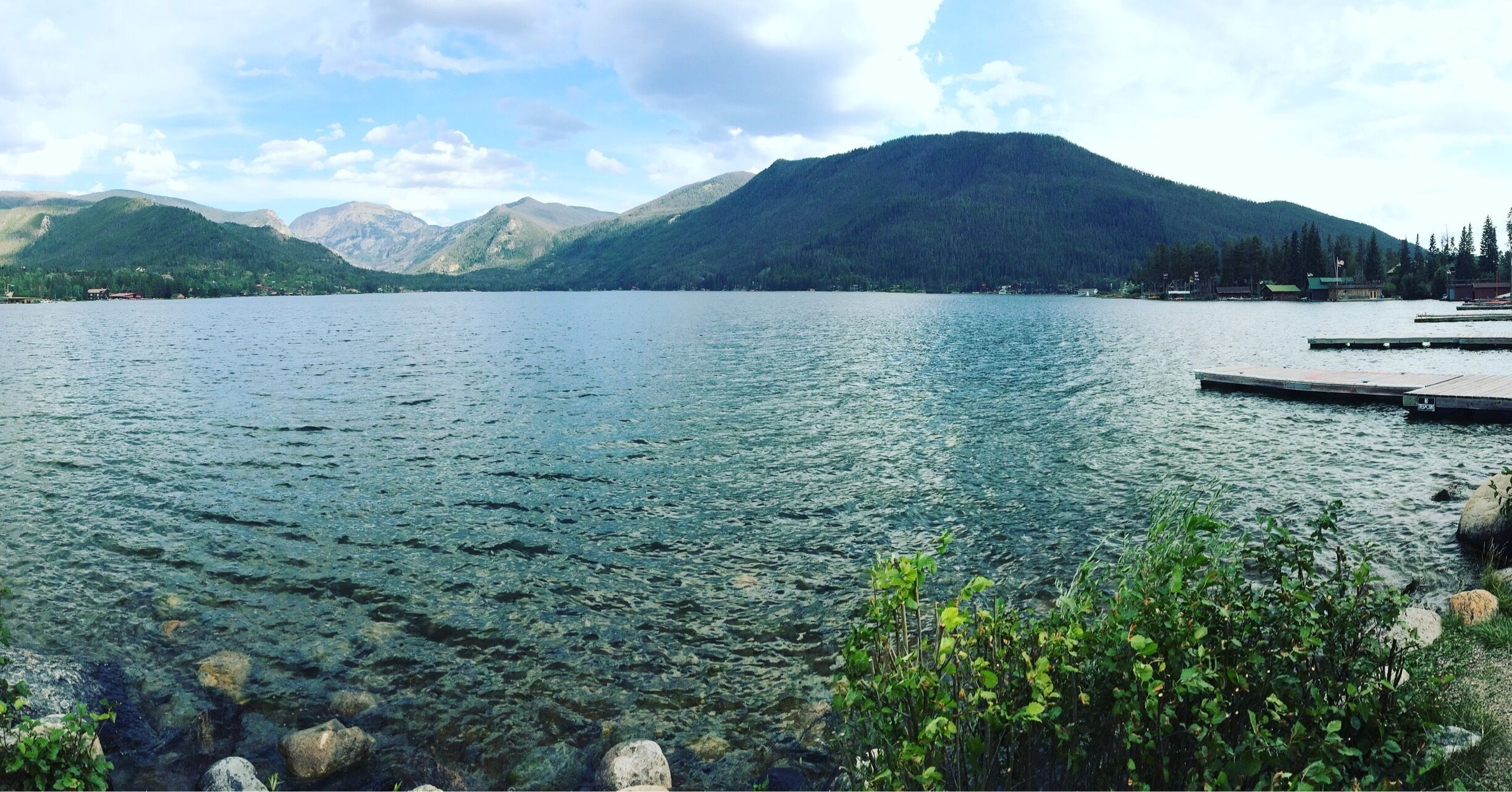 A calm lake with clear water, surrounded by mountains and a dock.