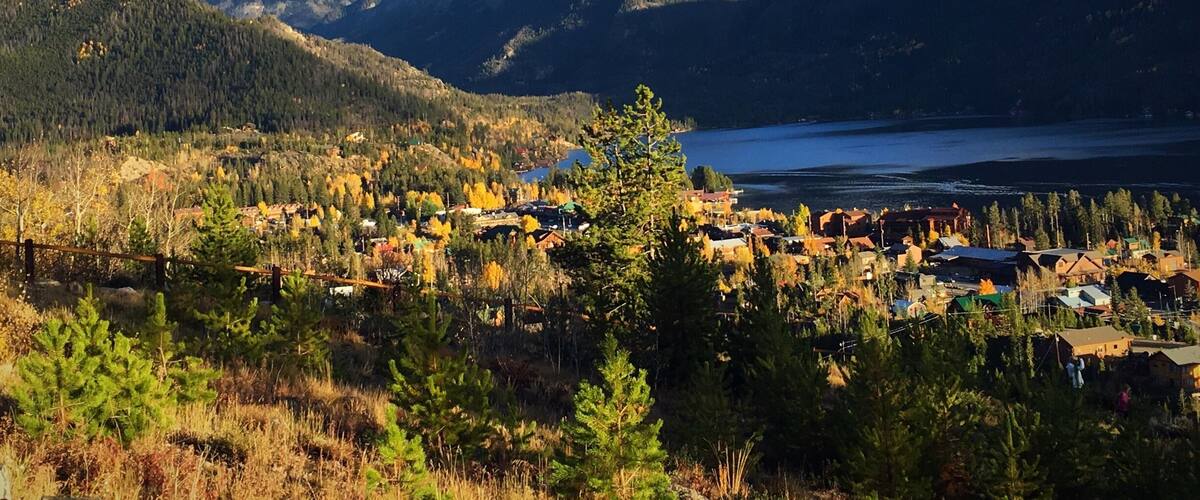 Un paisaje montañoso con un lago, árboles de colores otoñales y un pequeño pueblo.