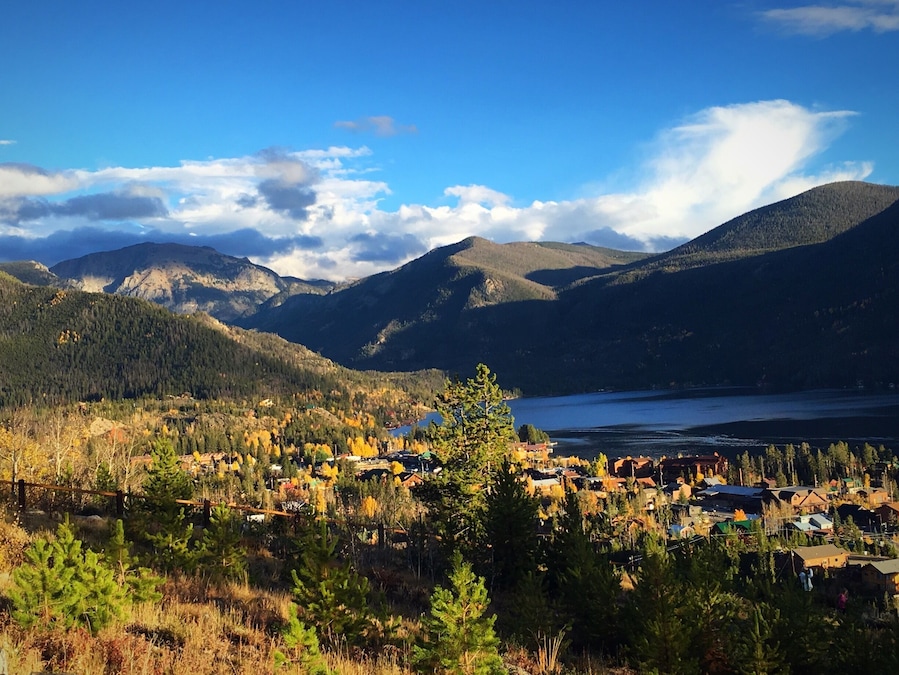 Un paisaje montañoso con un lago, árboles de colores otoñales y un pequeño pueblo.