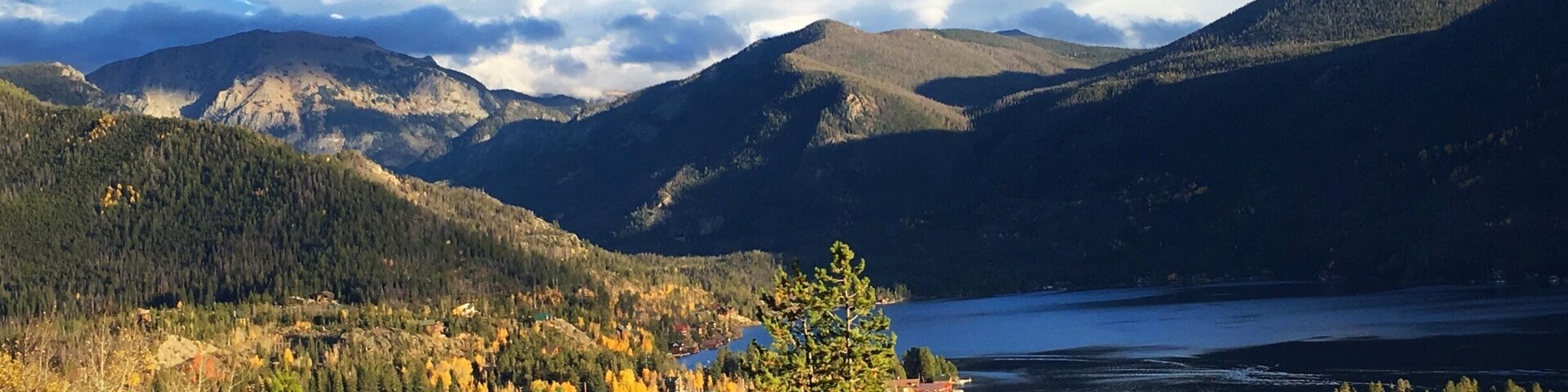 Un paisaje montañoso con un lago, árboles de colores otoñales y un pequeño pueblo.