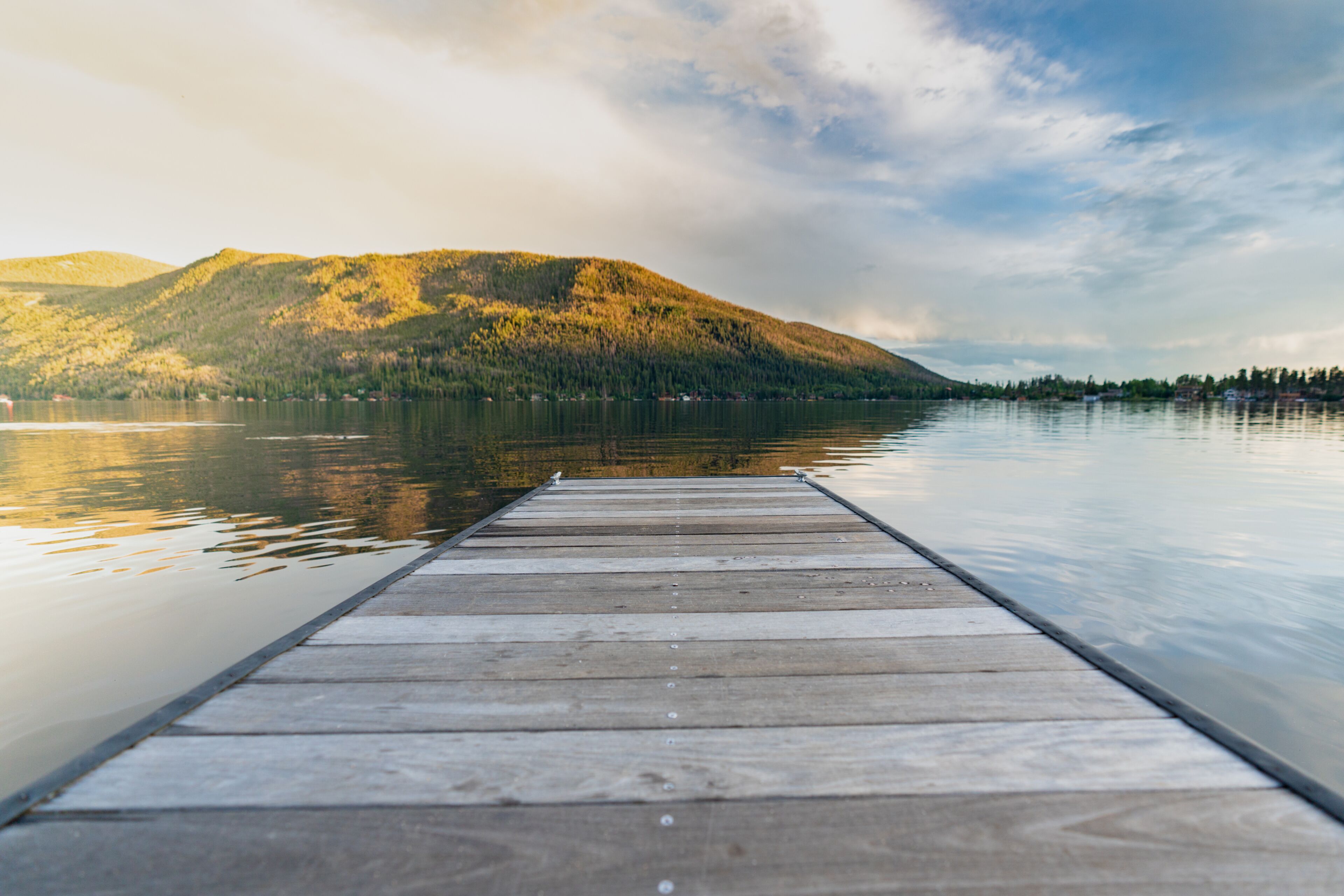 A wooden dock extending into calm water with a mountain in the background.