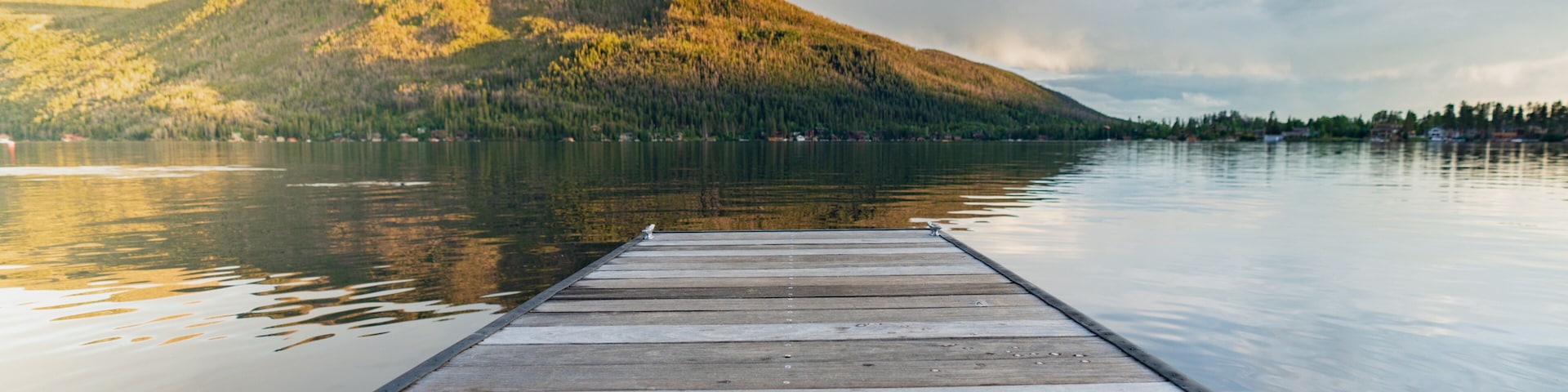 A wooden dock extending into calm water with a mountain in the background.
