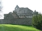 A historic stone castle with a large grassy lawn in front.