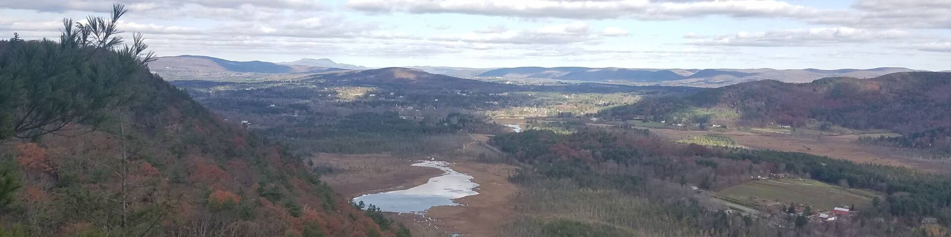 Un paysage montagneux avec une rivière, des arbres aux couleurs automnales et quelques bâtiments dispersés.
