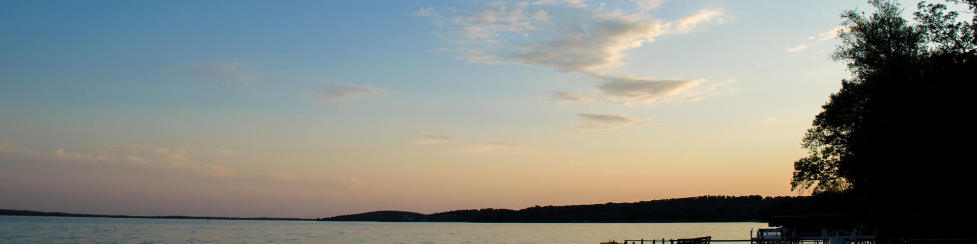 A calm lake at sunset with a wooden dock and benches.