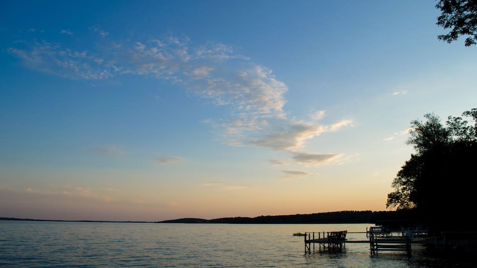 A calm lake at sunset with a wooden dock and benches.