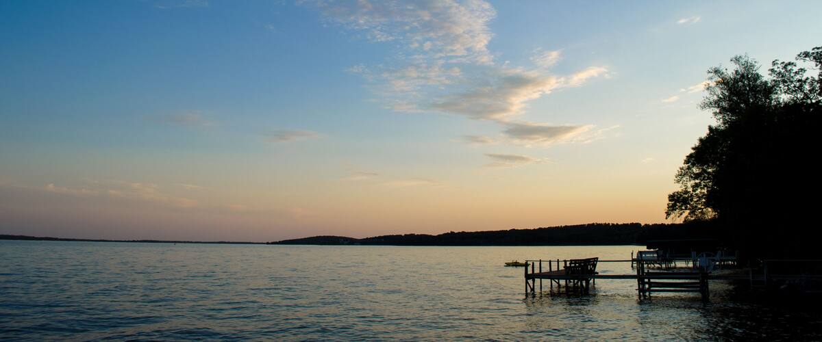 A calm lake at sunset with a wooden dock and benches.