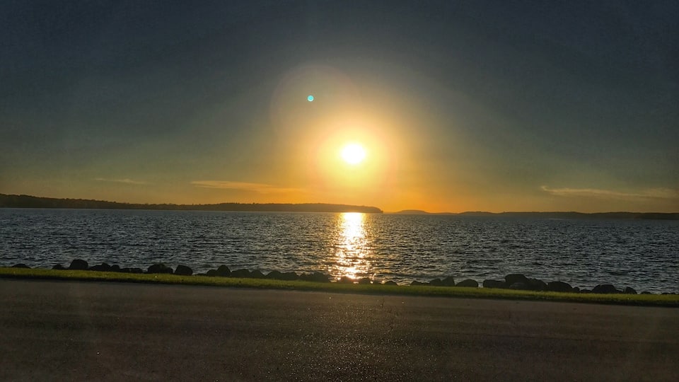 A sunset over a body of water with a road in the foreground.