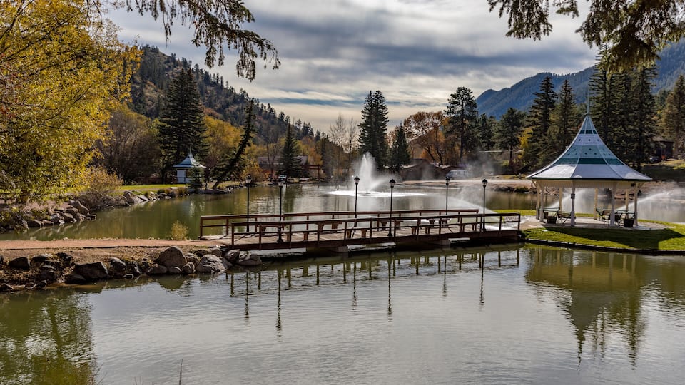 A tranquil lake with a wooden dock, a gazebo, and a fountain.