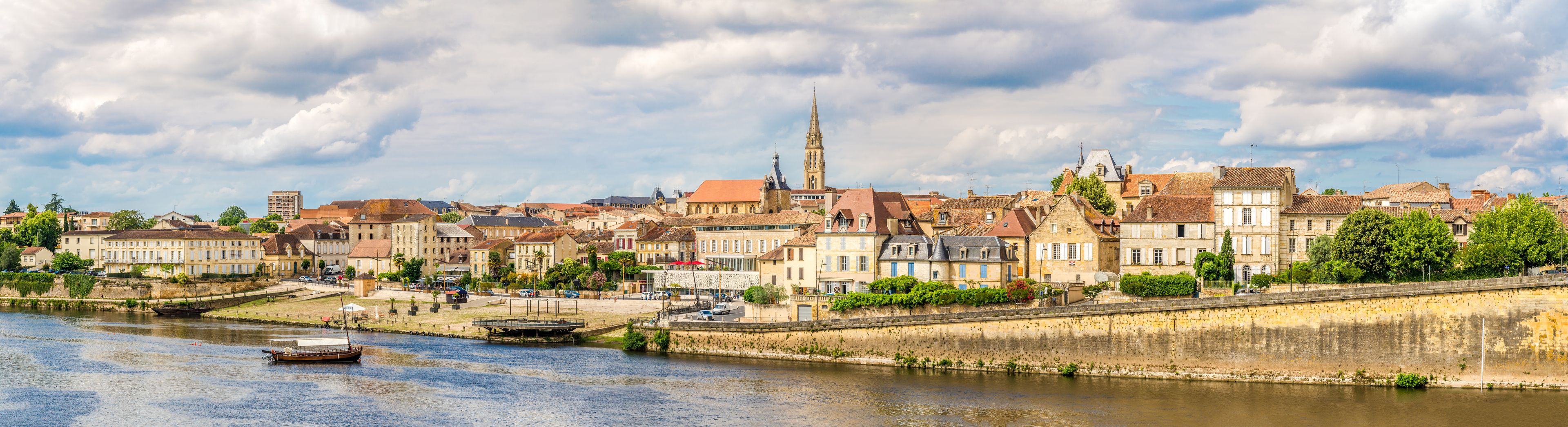 A riverside town with historic buildings, a prominent church tower, and a bridge.