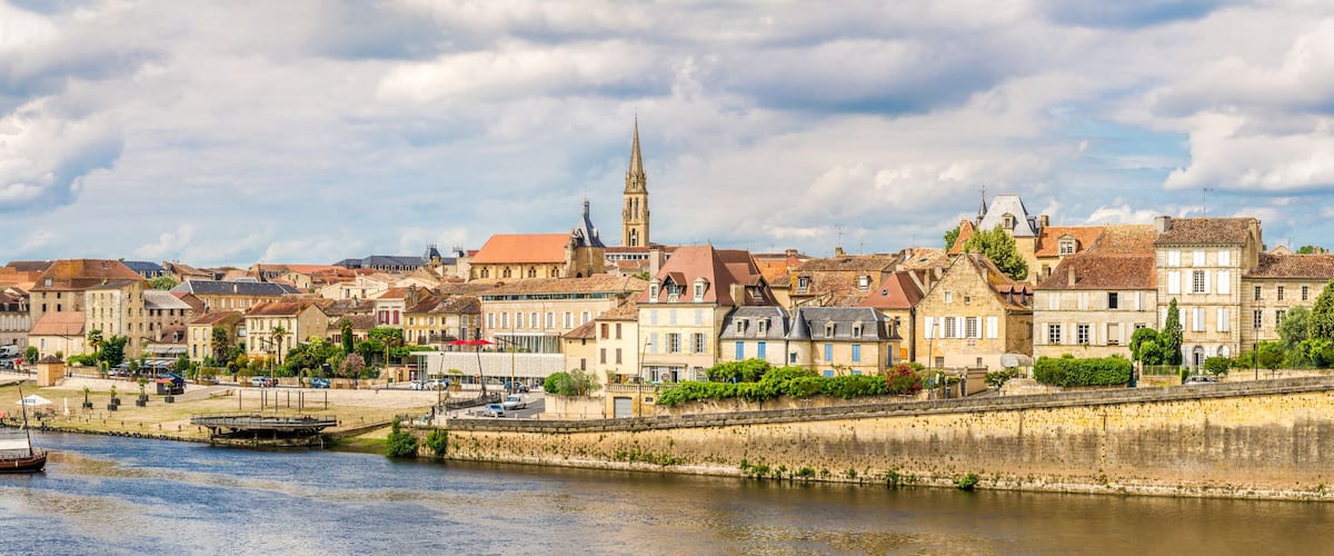 A riverside town with historic buildings, a prominent church tower, and a bridge.