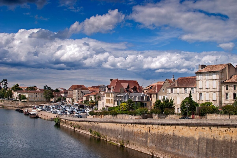 Ein Fluss mit einer Steinmauer und Gebäuden am Ufer.