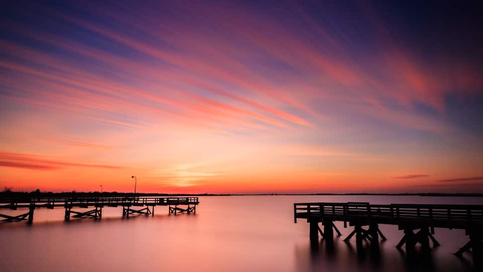 A pier extending into calm waters at sunset with a vibrant sky.