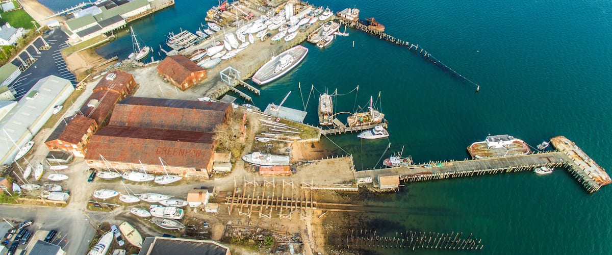 An aerial view of a harbor with boats, a ship, and a dock extending into the water.