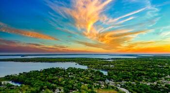 A coastal landscape with a lake, dense greenery, and a sunset sky.