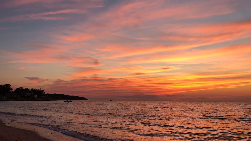 A beach with waves at sunset, a distant shoreline, and a clear sky.