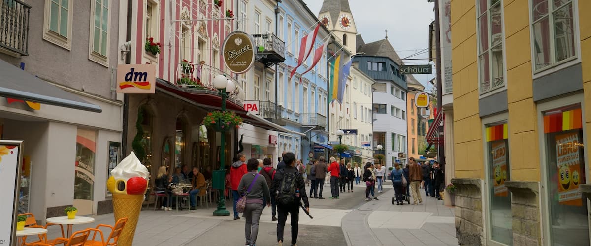 A bustling European street with historic buildings, a church spire, and various shops.