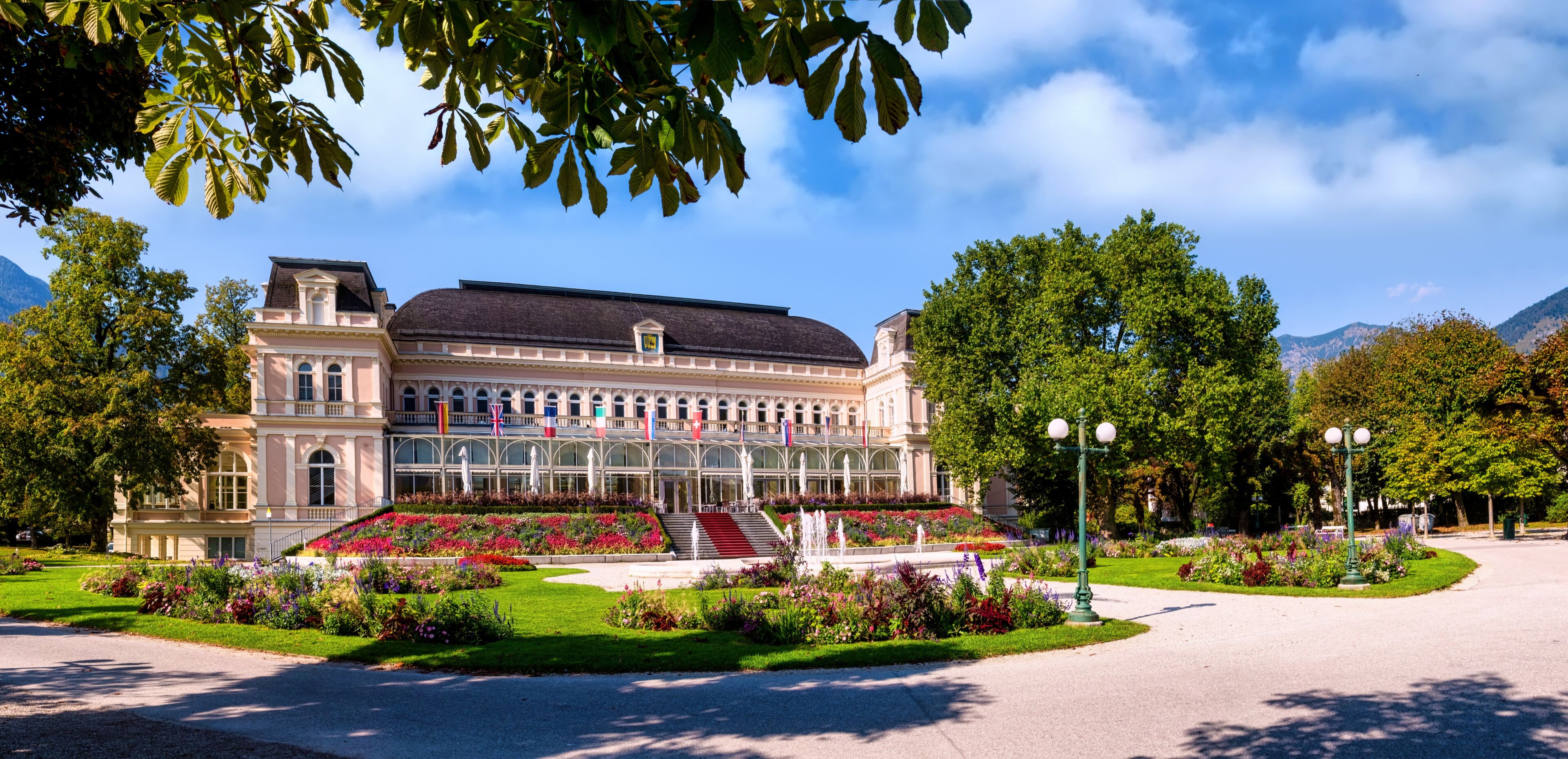 A grand building with a symmetrical facade, a central staircase, and a well-maintained garden with colorful flowers and a fountain.