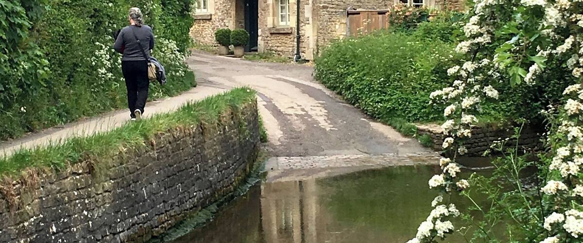A narrow waterway flanked by stone buildings with chimneys, surrounded by lush greenery and flowering plants.