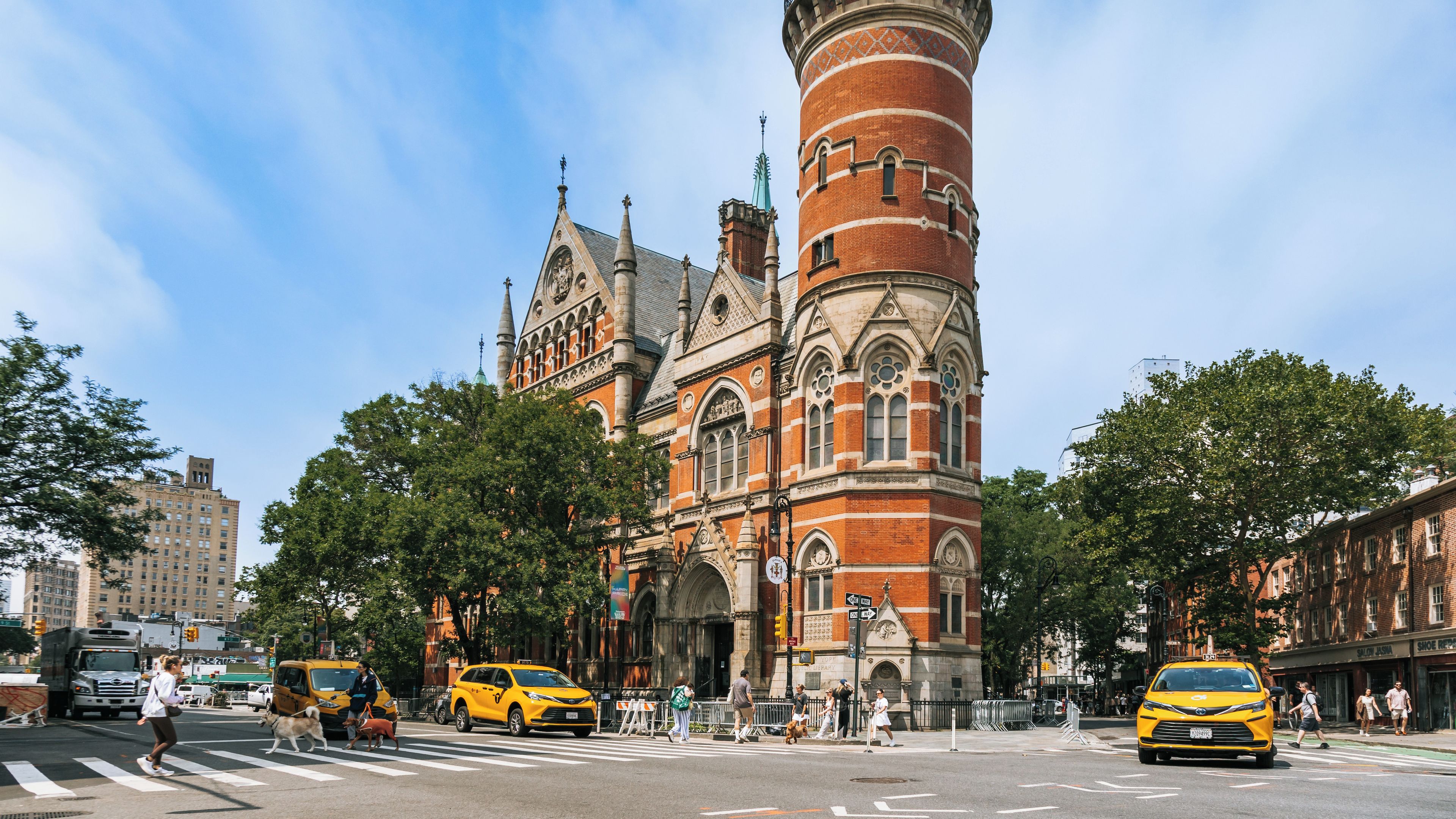 A historic building with a tall tower, surrounded by trees and modern vehicles.