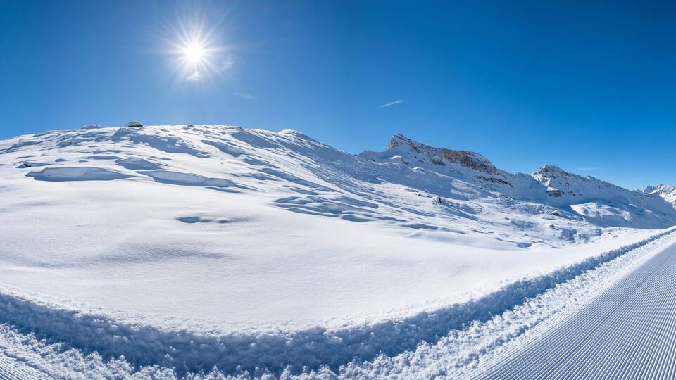 A snow-covered mountain path with tracks leading towards a peak under a clear blue sky.